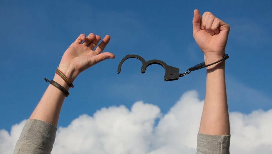 A woman with her hands in the air showing one hand free from handcuffs